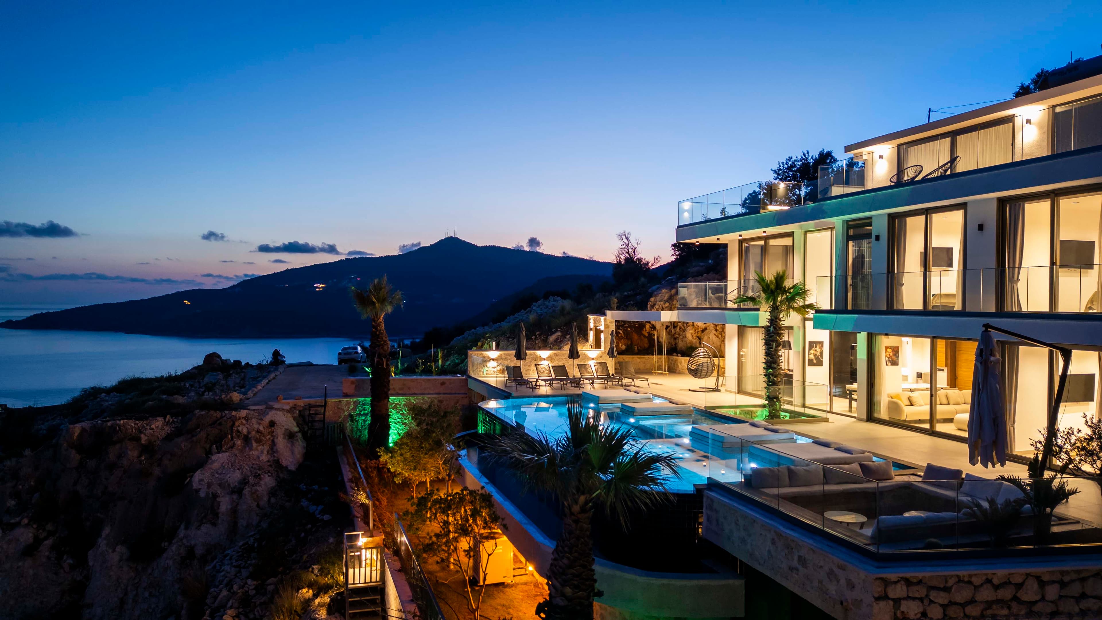 A modern cliffside villa at dusk, with an infinity pool and terrace overlooking the coast