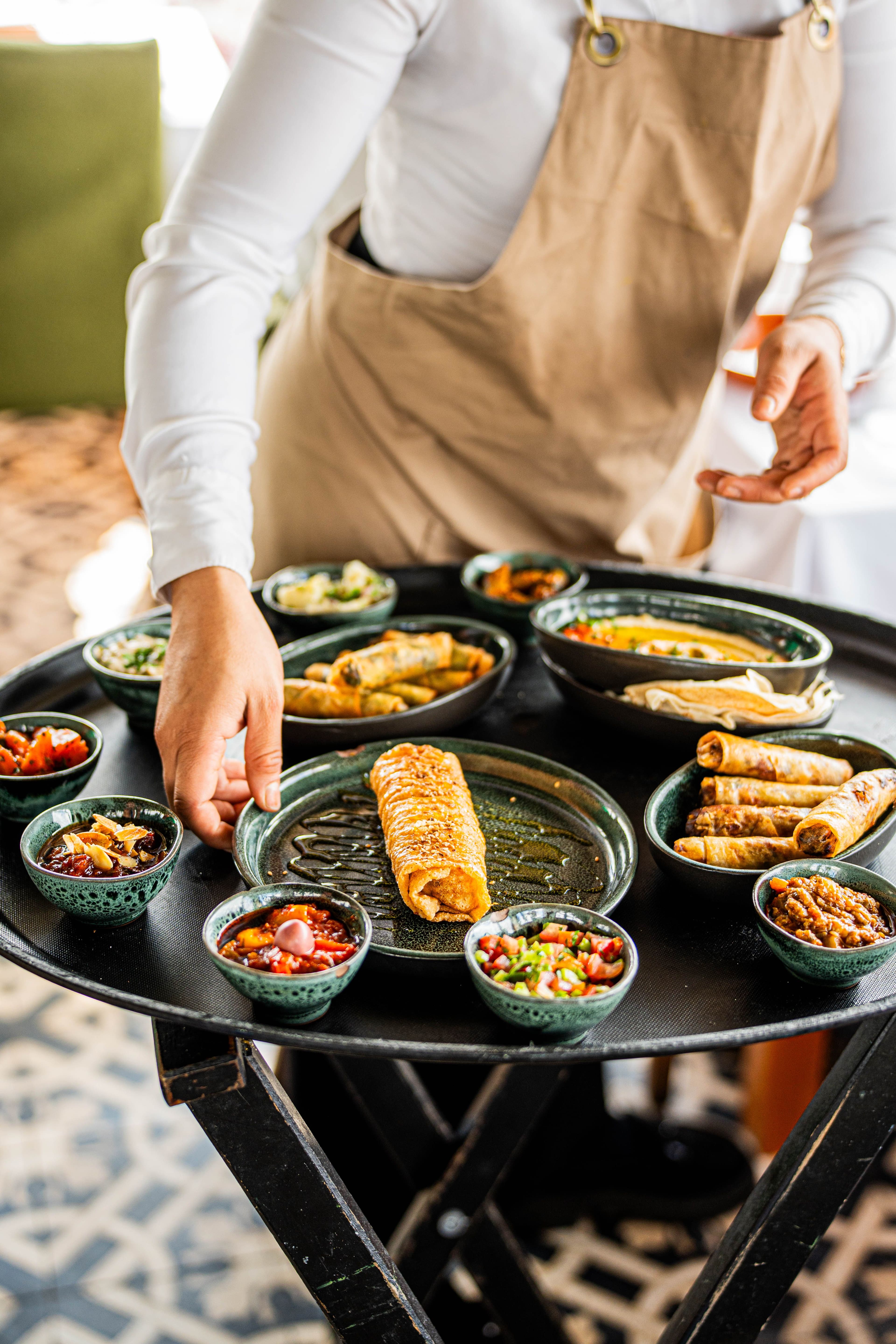 A server presenting a tray of Turkish mezze and appetizers at an outdoor table