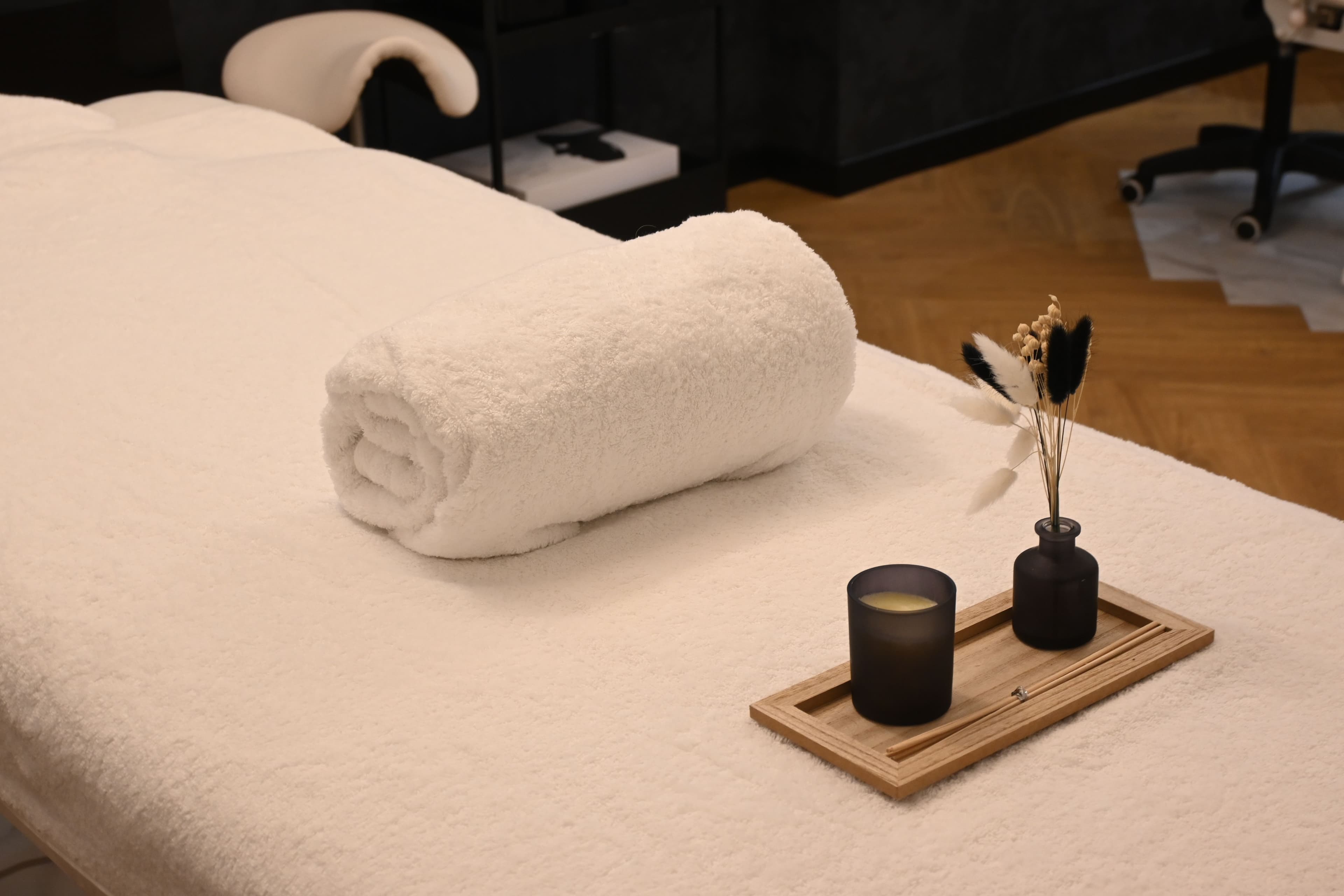 A rolled towel, candle, and dried flowers laid out on a treatment table in a quiet spa room